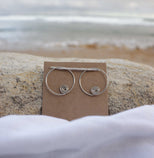 Silver hoop earrings on a brown card with a beach background