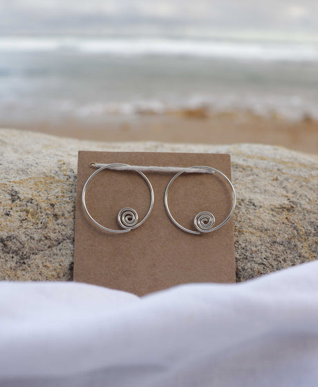 Silver hoop earrings on a brown card with a beach background
