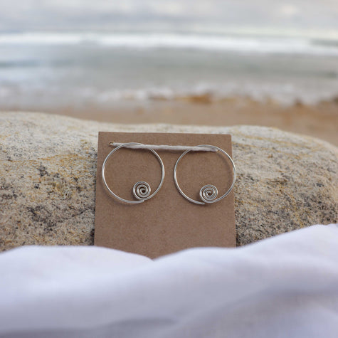 Silver hoop earrings on a brown card with a beach background