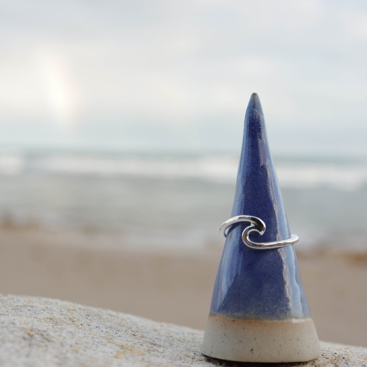 Silver wave ring on a blue ceramic cone with a beach background