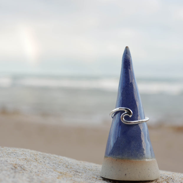 Silver wave ring on a blue ceramic cone with a beach background